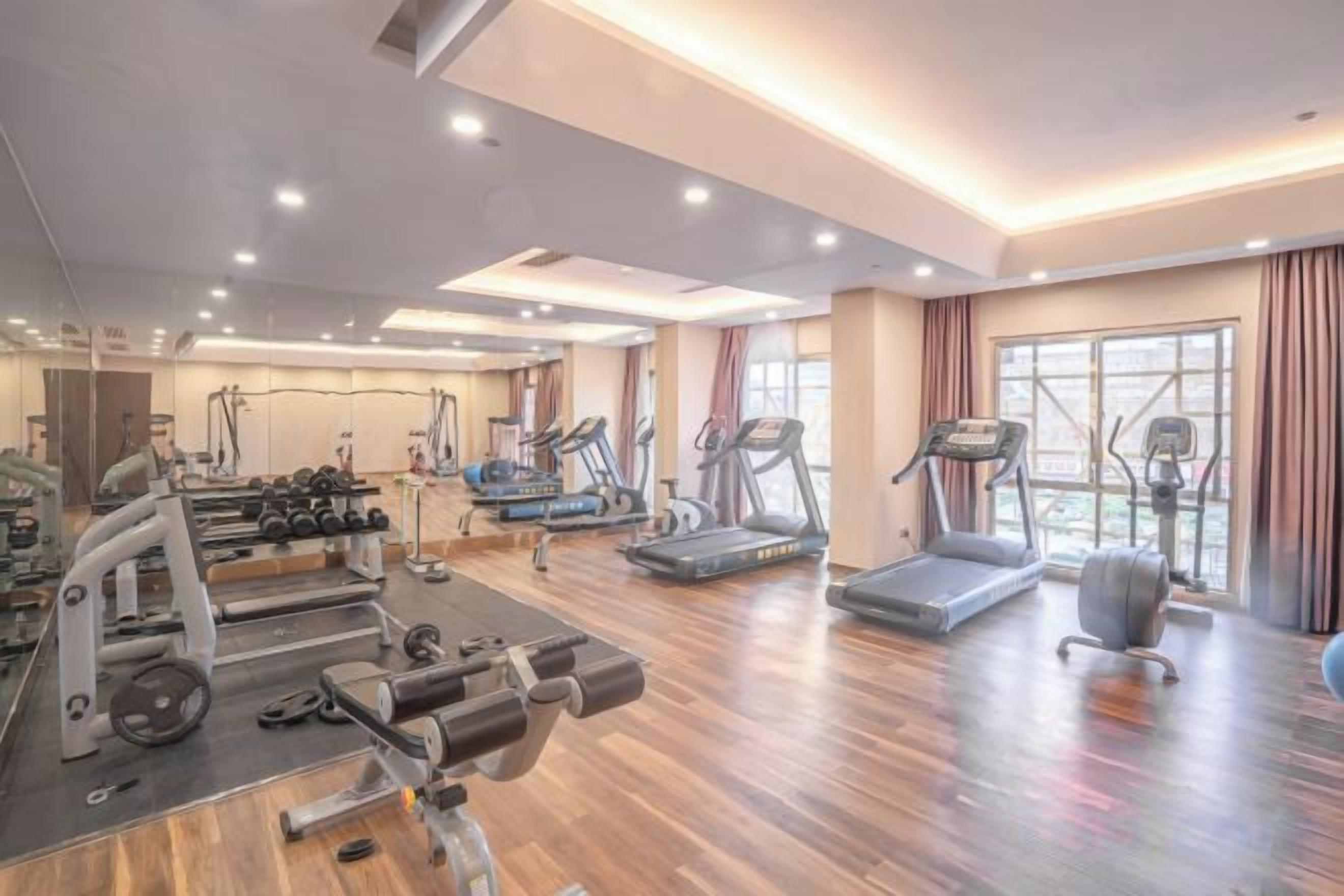 A spacious gym with cardio machines, free weights, and a mirrored wall.