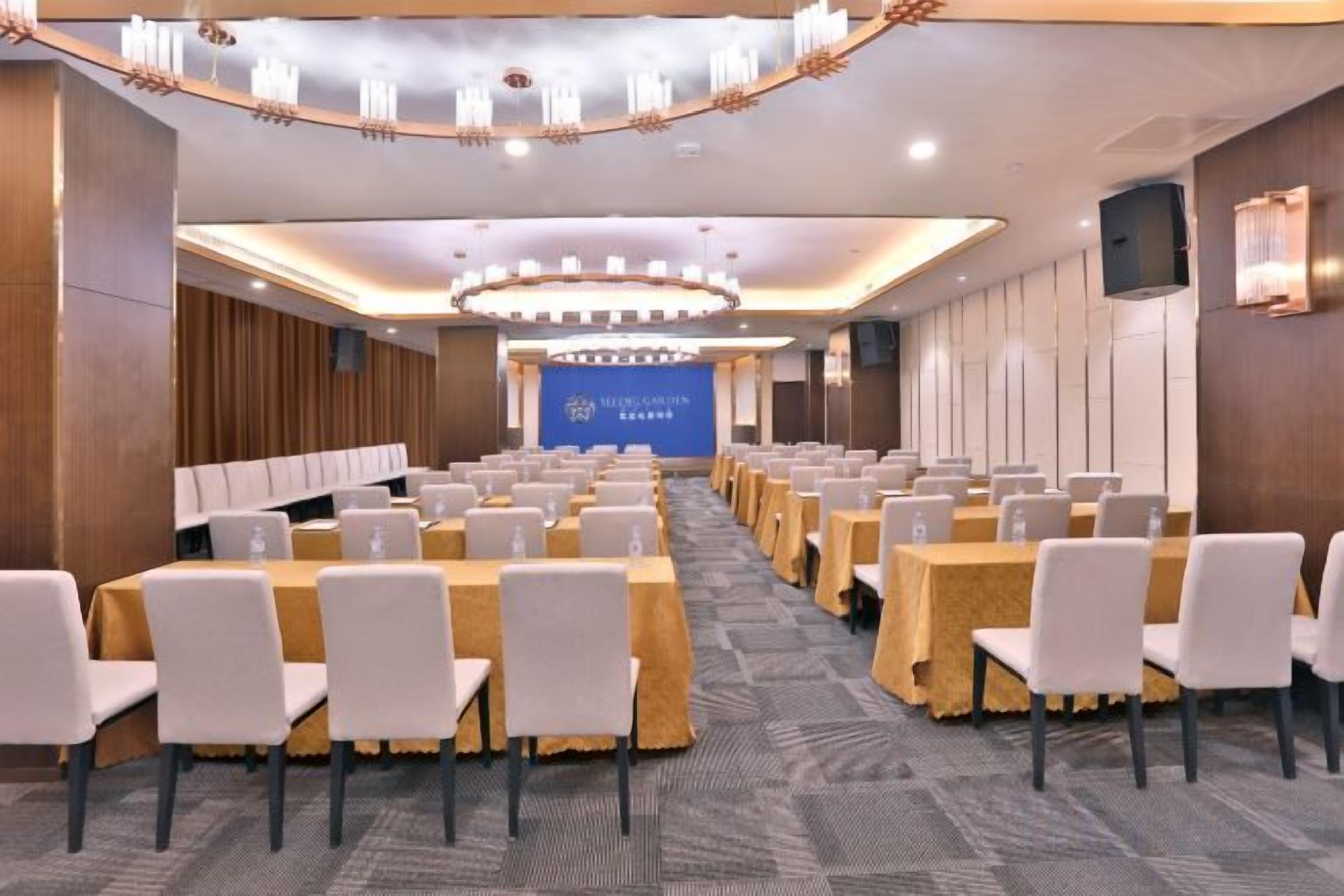 A conference room with rows of tables and chairs, a large screen at the front, and a chandelier.