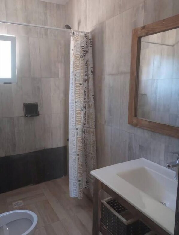 A bathroom with a shower curtain, a sink, and a mirror. - Hotel por día en general Acha  (General Acha)