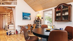 Een eethoek met een ronde tafel, bruine stoelen, een houten trap en een boekenkast.