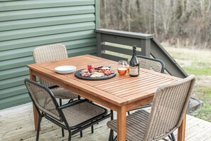 A wooden deck with a table set for a meal, including plates, cutlery, and a bottle. - Luxe Cottage w/ hot tub + firepit + library near lake. Pet friendly! (Lexington)