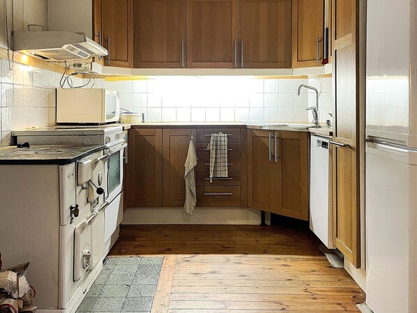Una cocina con gabinetes de madera, estufa, microondas y refrigerador.