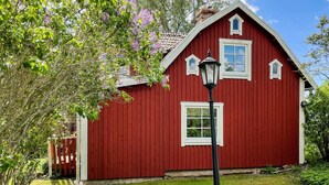 Une maison en bois rouge avec des bordures blanches, une petite fenêtre et un lampadaire devant.