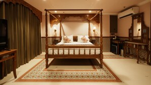 Un lit à baldaquin avec une structure en bois et une literie blanche, un téléviseur posé sur une table d’appoint et un tapis à motifs sur le sol.