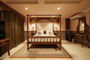 A four-poster bed with a wooden frame and white bedding, a television on a side table, and a patterned rug on the floor.