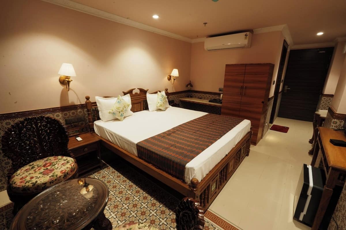 A hotel room with a large bed, two bedside tables, a chair, a small table, and a wardrobe.