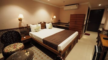 A hotel room with a large bed, two bedside tables, a chair, a small table, and a wardrobe.