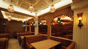Un restaurant avec des banquettes et des tables, des lustres décoratifs et des boiseries.