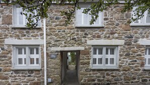 A stone cottage with a narrow entrance, white shutters, and a sign reading "Pilot's Cottage."