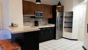 Una cocina compacta con armarios negros, un microondas, un refrigerador y una cafetera.