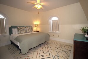 A bedroom with a bed, a nightstand, a lamp, a ceiling fan, and a window.
