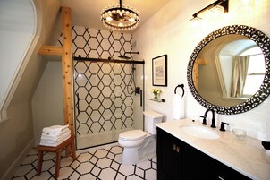 A bathroom with a geometric patterned floor, a round mirror with a leaf pattern, a white toilet, and a sink with a black faucet.