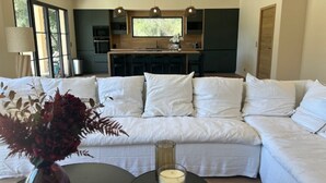 Un salon moderne avec un canapé d’angle, une table basse ornée d’une bougie et un vase rempli de fleurs.