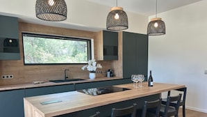Une cuisine moderne dotée d’un îlot central, de meubles de rangement aux couleurs sombres et d’un éclairage suspendu.