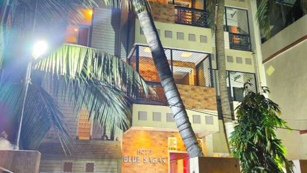 Un hotel de varios pisos con un balcón en el segundo nivel, palmeras y un letrero que dice "Hotel Blue Sagan".