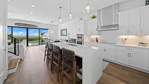A modern kitchen with white cabinetry, a large island with bar stools, stainless steel appliances, and pendant lighting. - 4-bedroom oceanfront villa in Melbourne Beach with (Melbourne Beach)
