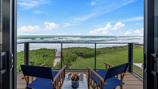A balcony with a view of the ocean, two blue chairs, and a table with a vase and two cups. - 4-bedroom oceanfront villa in Melbourne Beach with (Melbourne Beach)