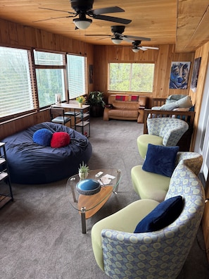 A cozy cabin interior with a round bean bag, a sofa, a glass coffee table, and a ceiling fan. - The Rock! 3 BR - 20 beds - 2 kitchens w/dock slip and awesome view of Mt Kineo (Rockwood)