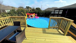 Terraza de madera con piscina, rodeada por un cerco de madera y equipada con una tumbona y una mesa.