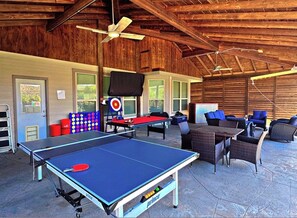 Un espacio recreativo al aire libre con mesas de ping pong, asientos y un dardo.