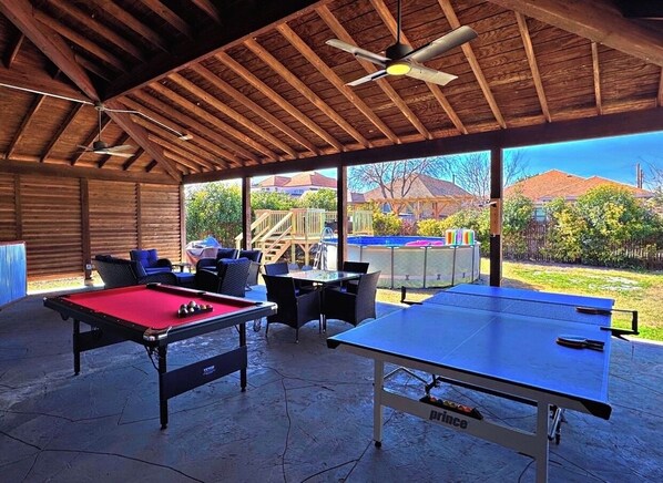 Un área recreativa al aire libre con mesa de billar, mesa de ping pong y mesa de futbolín.
