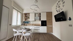 Una cocina moderna con armarios blancos, una mesa de comedor de madera con sillas y un televisor fijado a la pared.