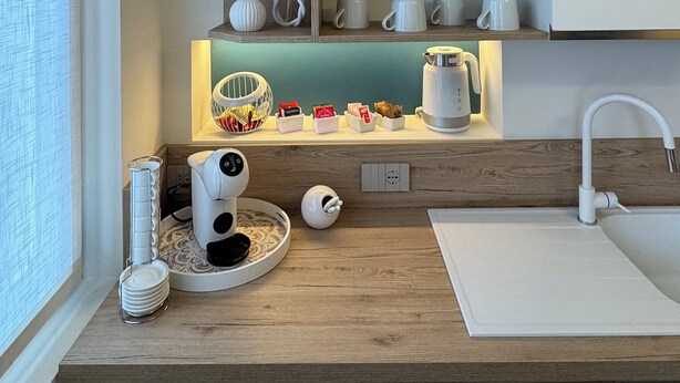 Una cocina moderna con estantes de madera, electrodomésticos blancos y una ventana con persianas.