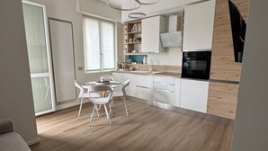 Una cocina moderna con armarios blancos, encimera de madera y horno empotrado. Hay un comedor con una mesa y sillas.