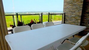 A dining area with a white table and chairs, a stone wall, and a view of a green field. - Kenting Green Yard Hostel (Pingtung)