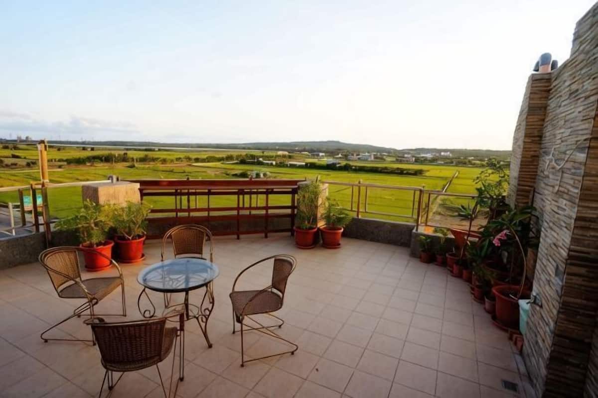 Une terrasse avec des chaises en osier, une table en verre, des plantes en pot et une vue sur un paysage verdoyant.