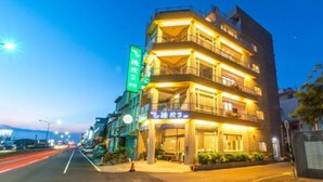 A multi-story hotel with a ground-level restaurant, illuminated balconies, and a green sign indicating a restaurant on the second floor. - Kenting Green Yard Hostel (Pingtung)