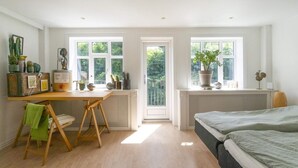 A bright, airy room with a wooden desk, a bed, and large windows offering a view of greenery outside. - 4 Star Holiday Home in Dybvad (Dybvad)