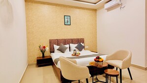 Une chambre d’hôtel avec un lit, deux chaises, une petite table avec des fruits, un climatiseur et un tableau au mur.