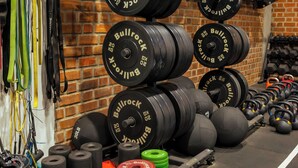 Une salle de sport équipée de divers appareils de musculation, notamment des haltères et des kettlebells, disposés le long d’un mur en briques.