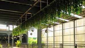 Un vaste espace intérieur doté de longues tables et de chaises, entouré de grandes fenêtres et agrémenté de plantes suspendues.