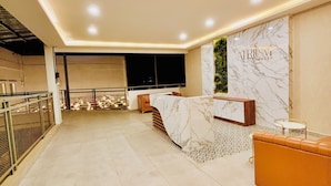 Un hall d’hôtel avec un comptoir de réception en marbre, un coin salon comprenant un canapé et une petite table, et une grande fenêtre donnant sur la rue.