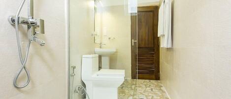 Un baño con cabina de ducha de vidrio, inodoro blanco y puerta de madera.