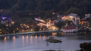 A lakeside view of a historic building complex with multiple structures, including a prominent white building with a red roof, surrounded by trees and illuminated by ambient lighting.