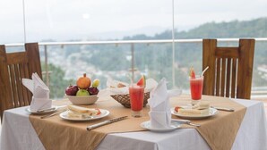 A table set with a fruit bowl, sandwiches, and drinks, overlooking a scenic view.