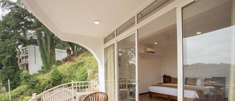 Un balcón con mobiliario de madera, una cama y vistas a zonas verdes y edificios.