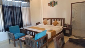 Habitación de hotel con cama, dos sillas, una mesita, una mesita de noche y un baño visible a través de una puerta abierta.