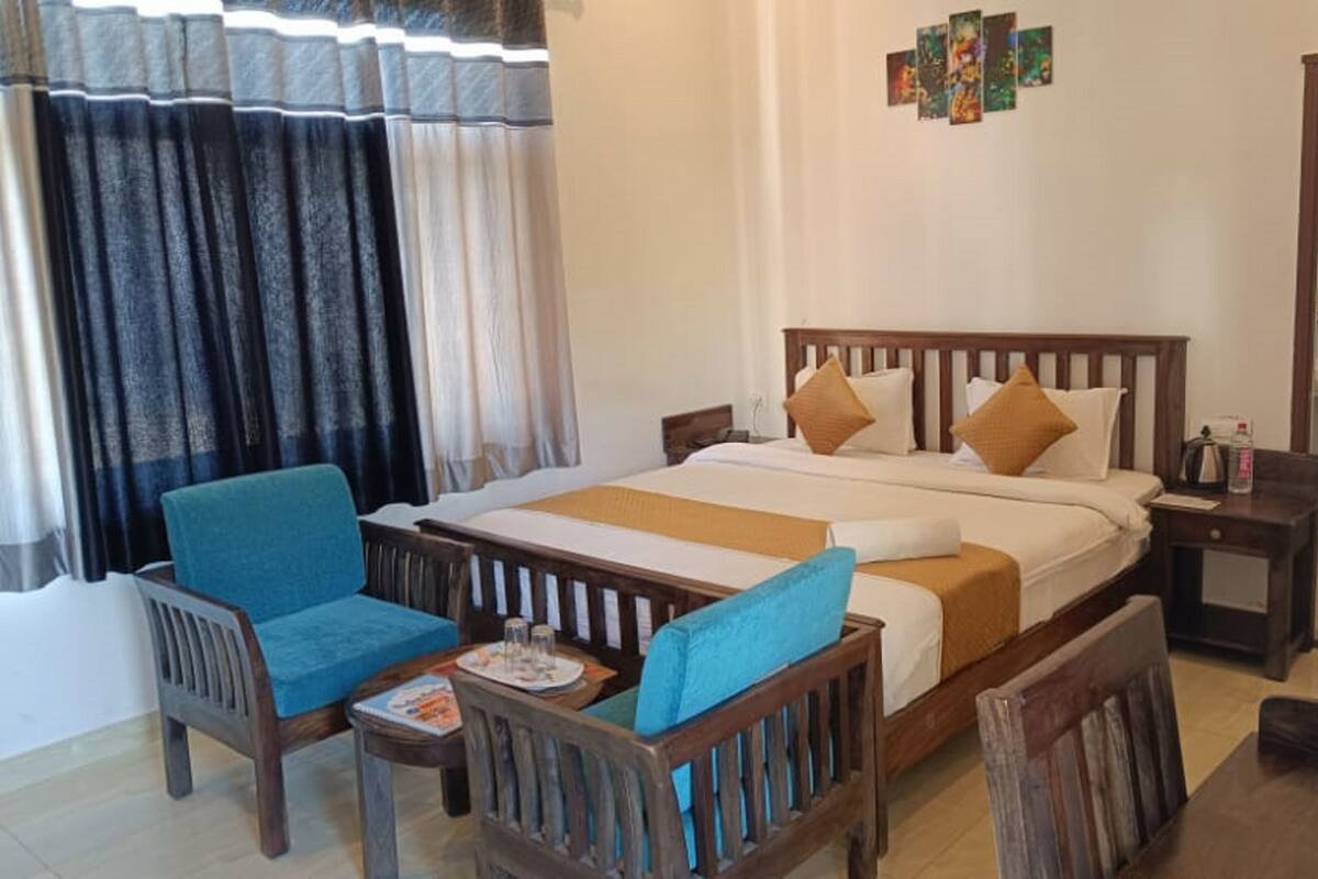A hotel room with a bed, two chairs, a small table, a nightstand, and a bathroom visible through an open door.