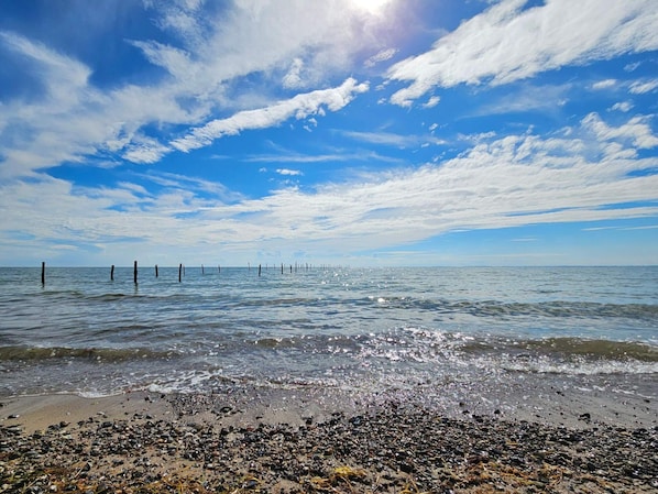 A beach with pebbles, a clear sky, and a calm sea.