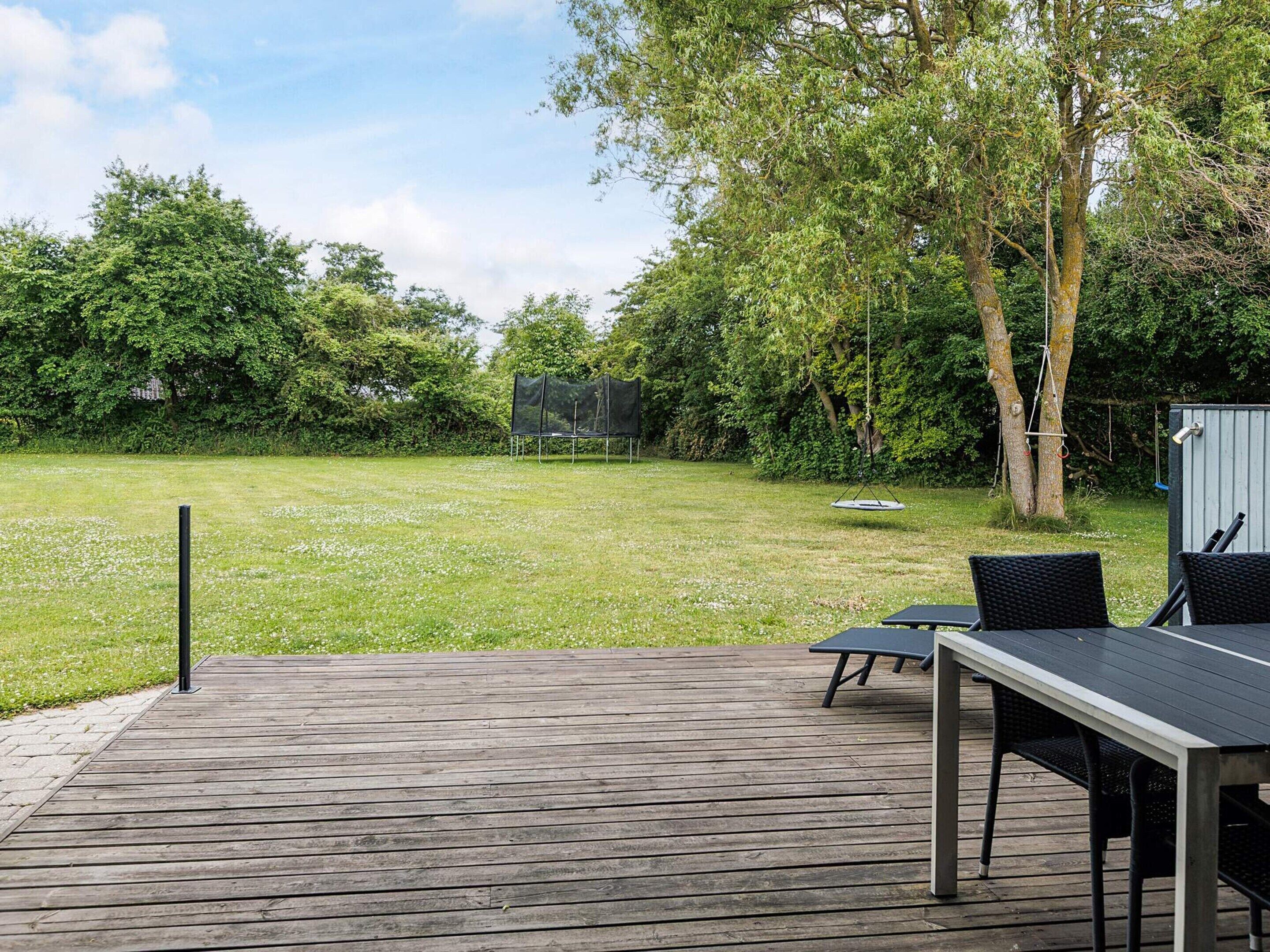 Une terrasse en bois avec une table et des chaises, entourée d’une pelouse et d’arbres.