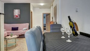 Una sala de estar con un sofá, una mesa de centro, una mesa de comedor con copas de vino y una botella de vino.