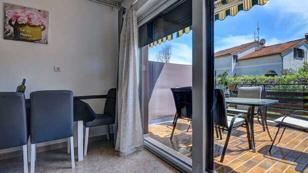Una habitación con puerta corrediza de vidrio que da a un patio exterior con sillas y una mesa.