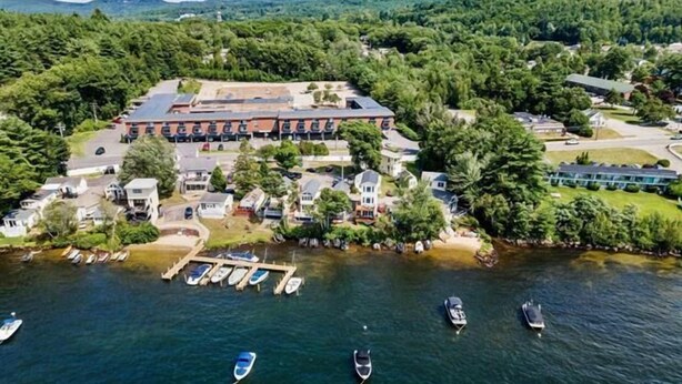 An aerial view of a lakeside property with a large building, docked boats, and surrounding greenery.