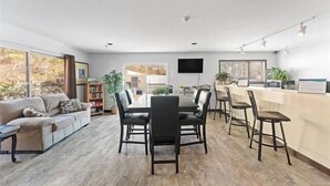A modern living room with a sofa, dining table, and chairs. There is a kitchen area with a counter and stools.