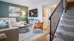 Un salon comprenant un canapé, une table basse et un fauteuil. Un escalier avec une rampe mène à une autre pièce.