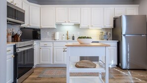 Une cuisine moderne avec des meubles blancs, des appareils en acier inoxydable et un plan de travail en bois.